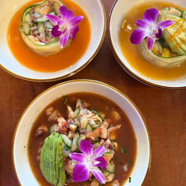 Three aguachiles in red, mango, and tamarindo broths topped with avocado and purple orchids.