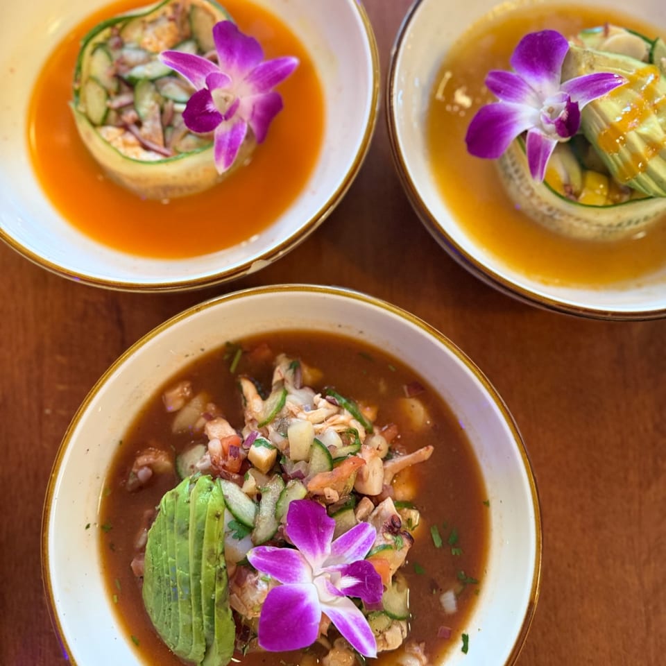 Three aguachiles in red, mango, and tamarindo broths topped with avocado and purple orchids.