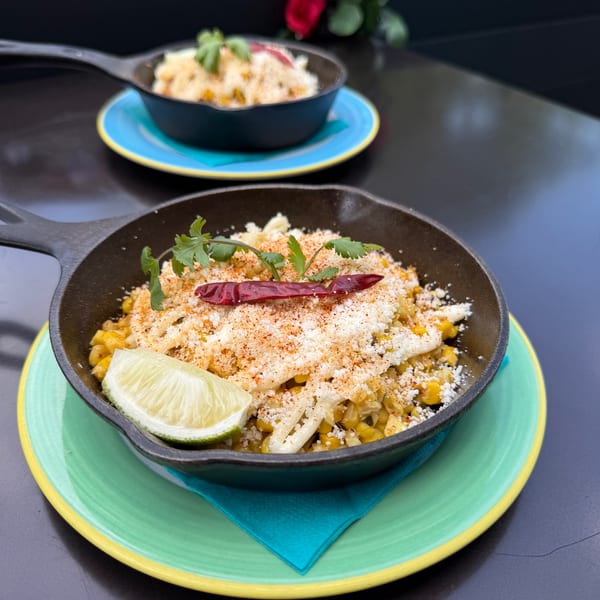 Mexican street elote in a cast iron skillet with cotija, chile de arbol, and lime.