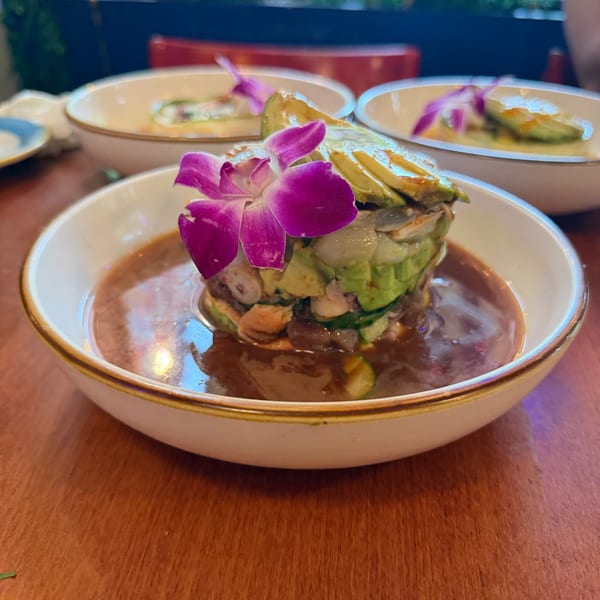 Shrimp and octopus ceviche with avocado and orchid in a white bowl.